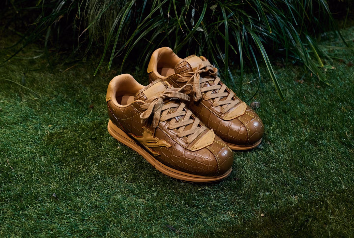 Pair of Tan Louis Vuitton sneakers with tan laces, set against a natural green grass background with outdoor lighting