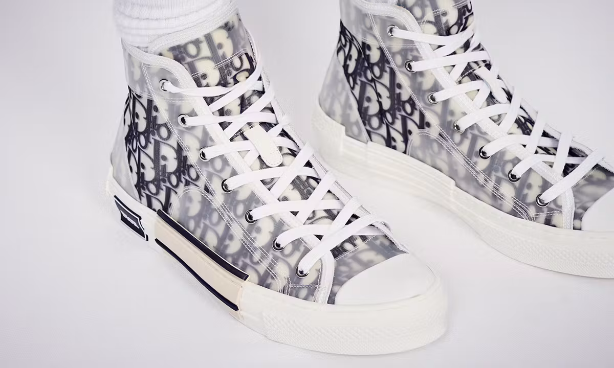 Close-up on-foot shot of a pair of Dior B23 high-top sneakers; features black and white Dior Oblique monogram canvas layered under a clear translucent upper film